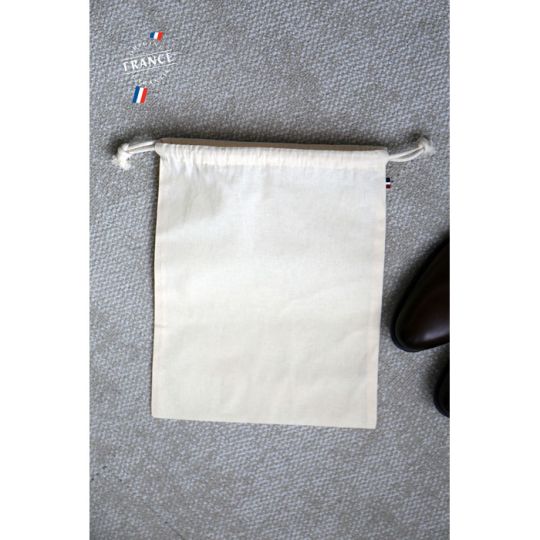 Pochon coton bio personnalisé écru à double cordon posé sur un sol gris près d'une chaussure en cuir