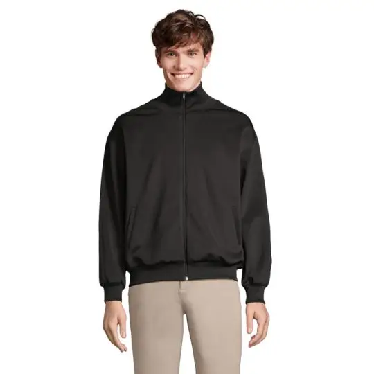 Veste de survêtement personnalisée JUNIOR noire zippée à col montant, portée sur un pantalon beige, vue de face