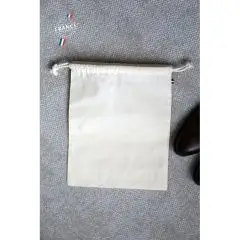 Pochon coton bio personnalisé écru à double cordon posé sur un sol gris près d'une chaussure en cuir